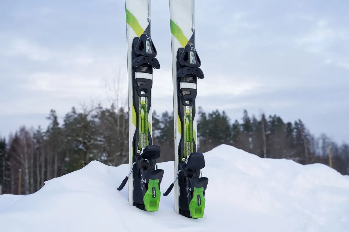 A pair of skis standing upright in a snowbank with pines behind