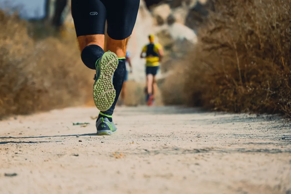 Low view of a trail runner’s legs and shoes on a dusty mountain trail